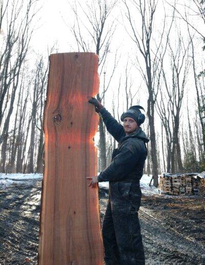 man stands next to a beautiful slab of freshly sliced wood that stands over 8 feet high
